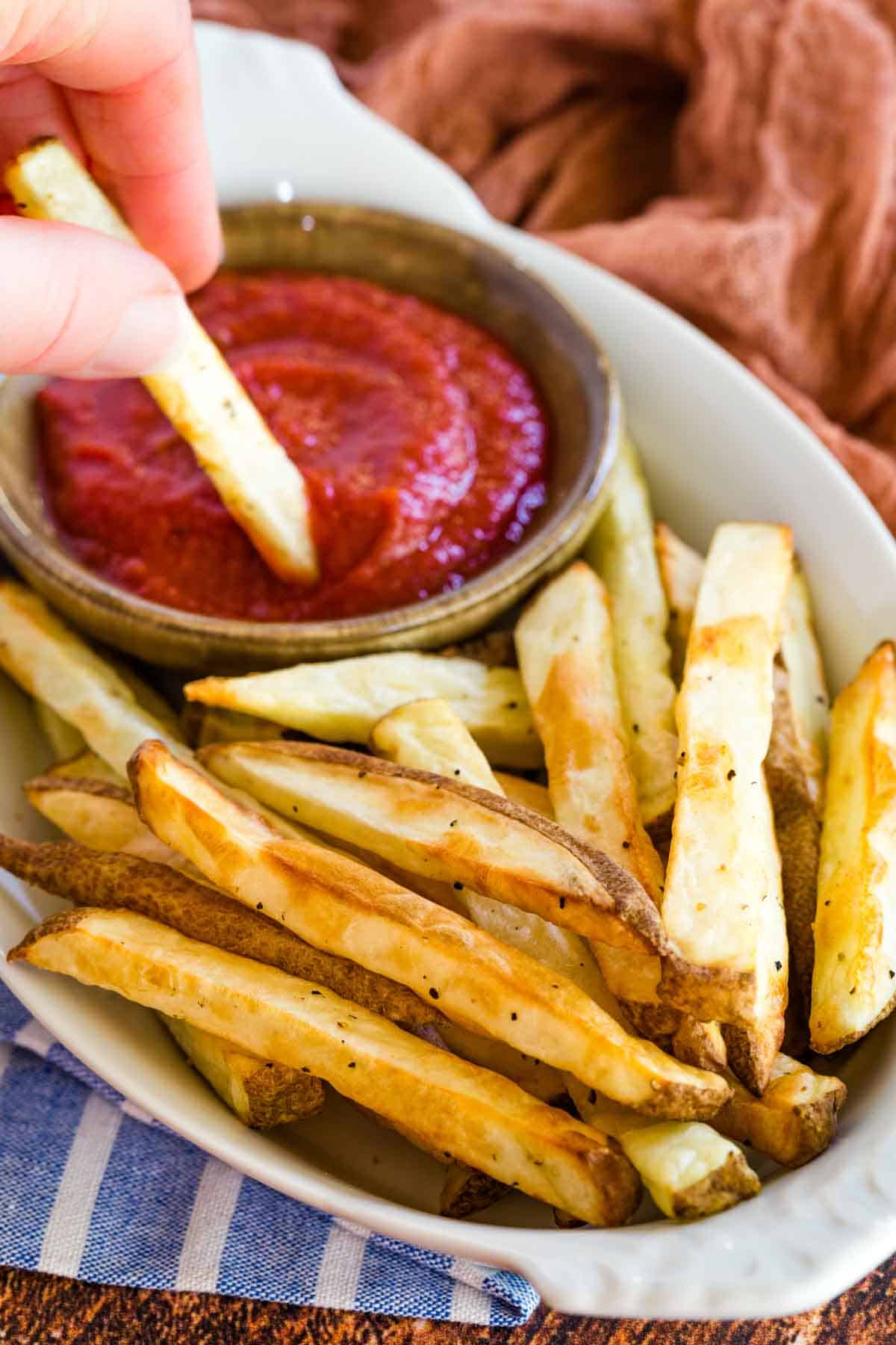 french fries in a white dish with one being dipped in a small bowl of ketchup