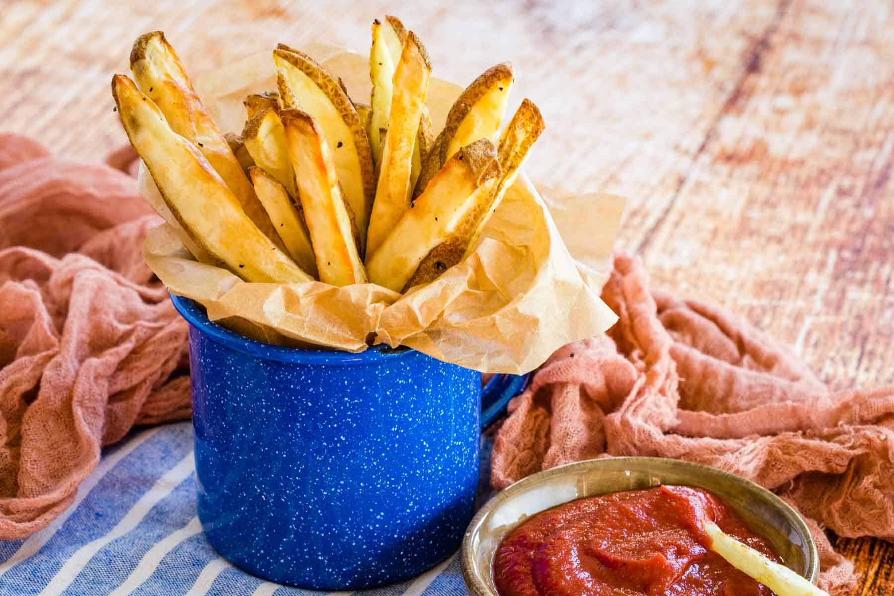 air fryer french fries in a blue cup next to a dish of ketchup