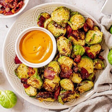 a plate of roasted brussels sprouts with bacon and a small bowl of dip