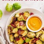 Air Fryer Brussels sprouts with bacon and parmesan on a plate with a small bowl of a dipping sauce