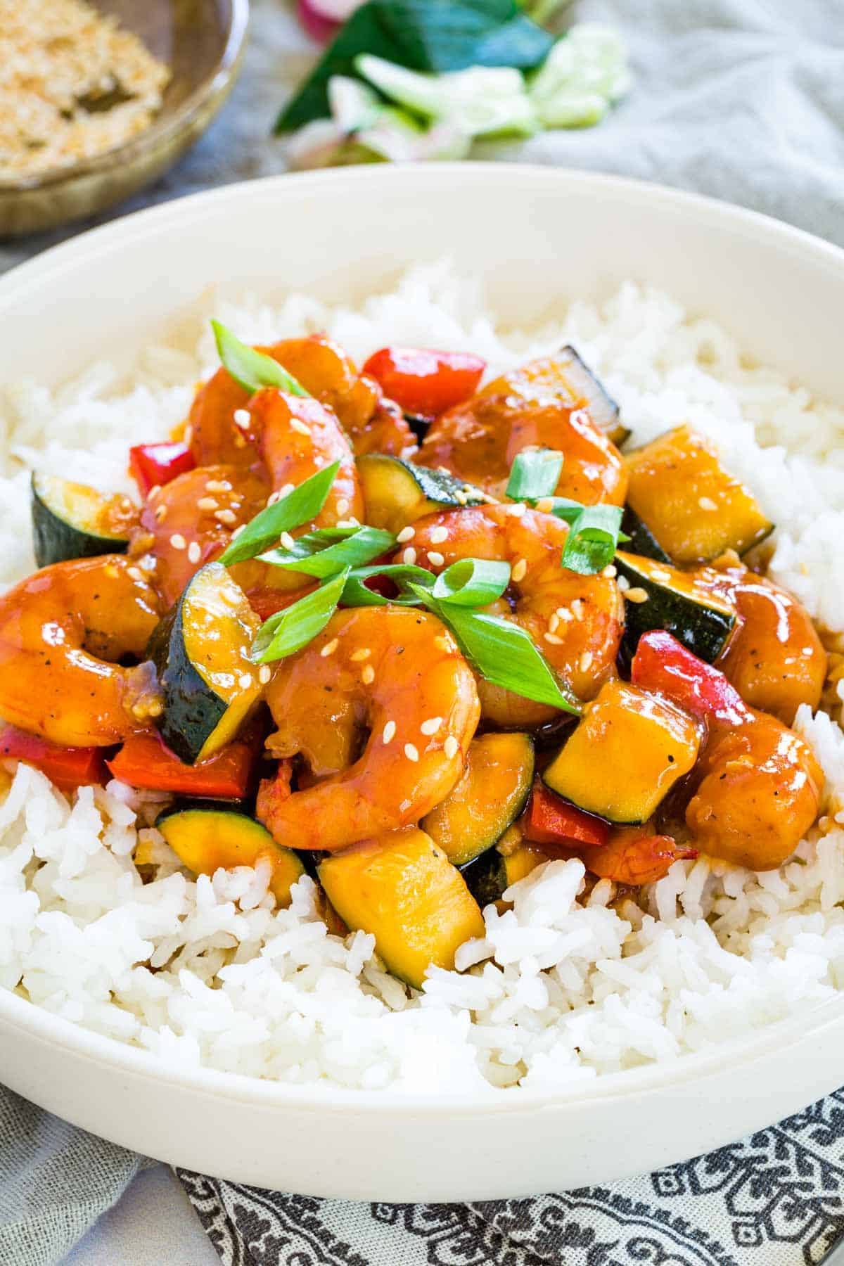 bourbon shrimp with vegetables in a thick sauce over white rice and garnished with sliced green onions and sesame seeds