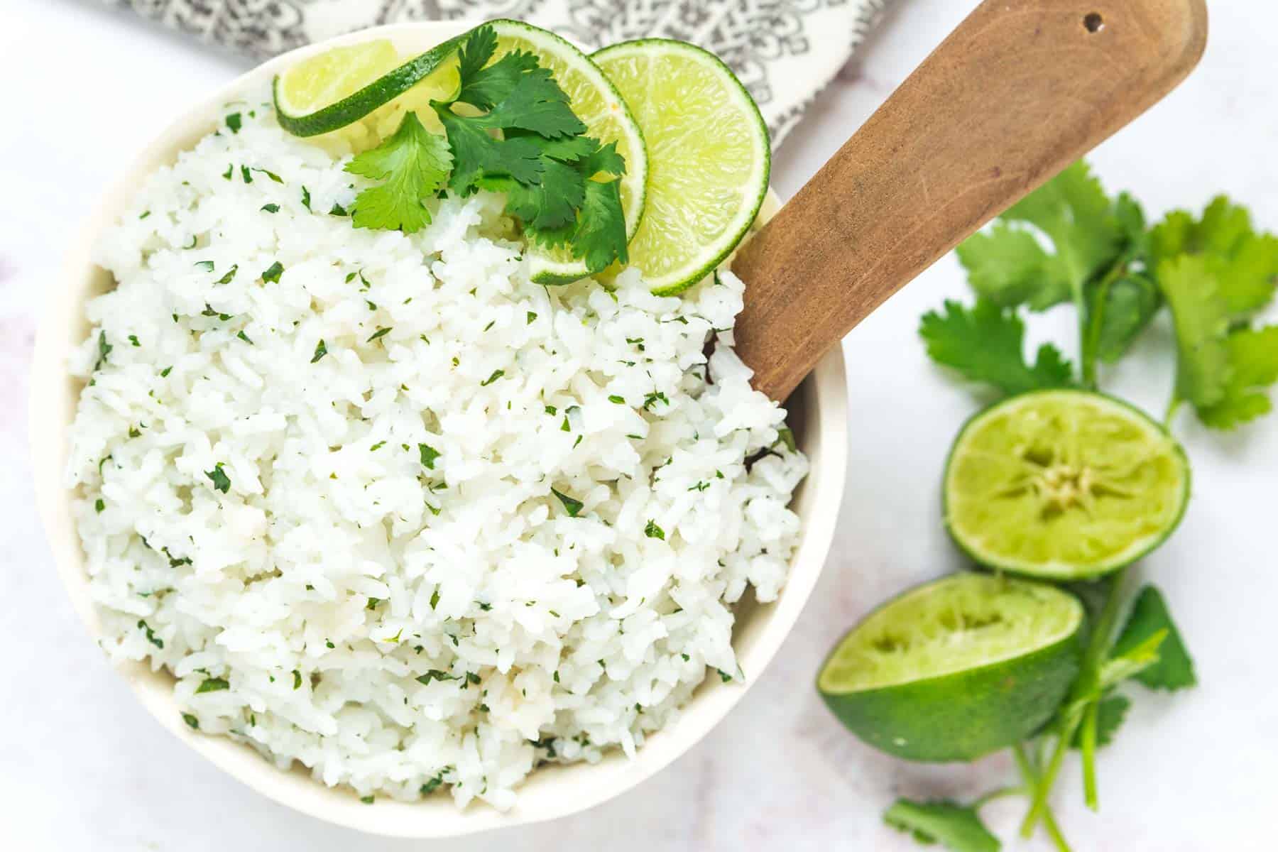 cilantro lime rice in a bowl with a serving spoon garnished with a sprig of cilantro and lime slices