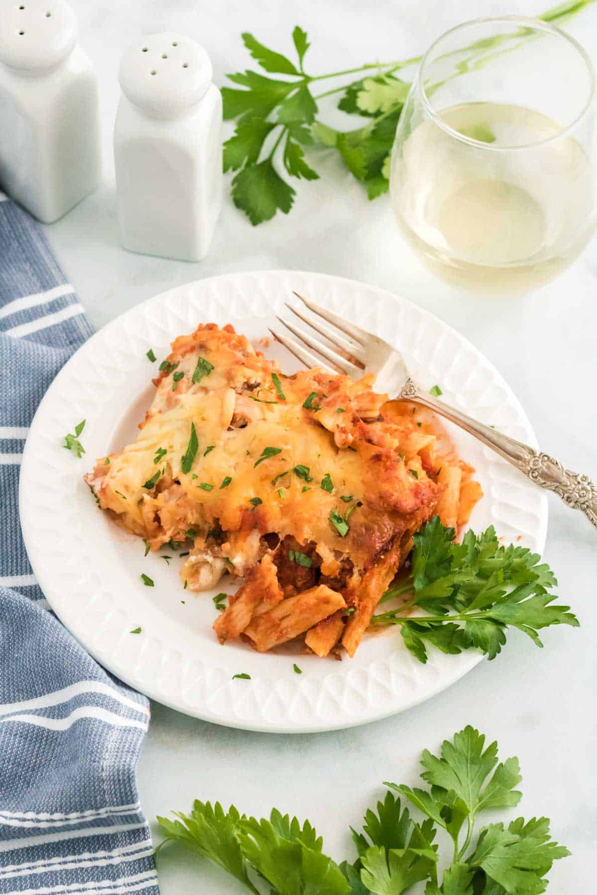 A serving of baked ziti on a plate garnished with fresh herbs.