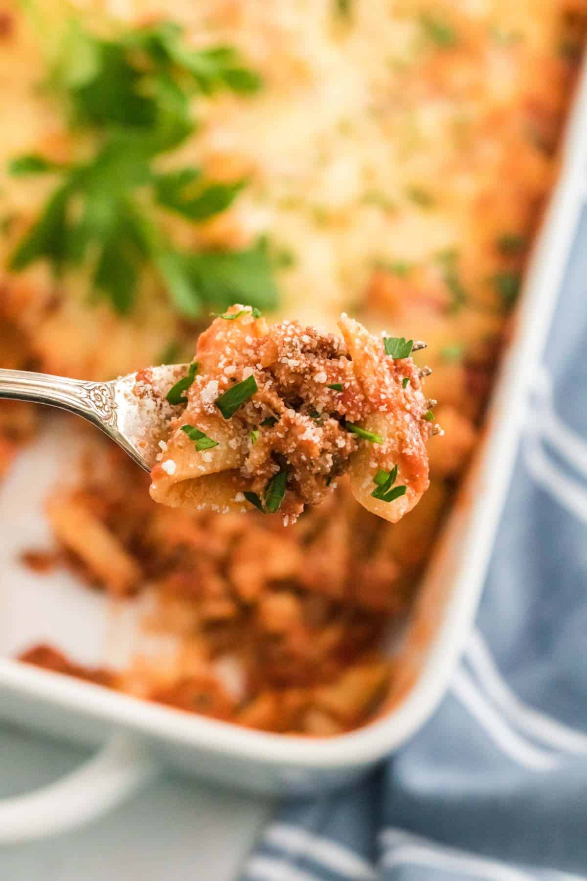 A forkful of baked ziti with the casserole in the background.