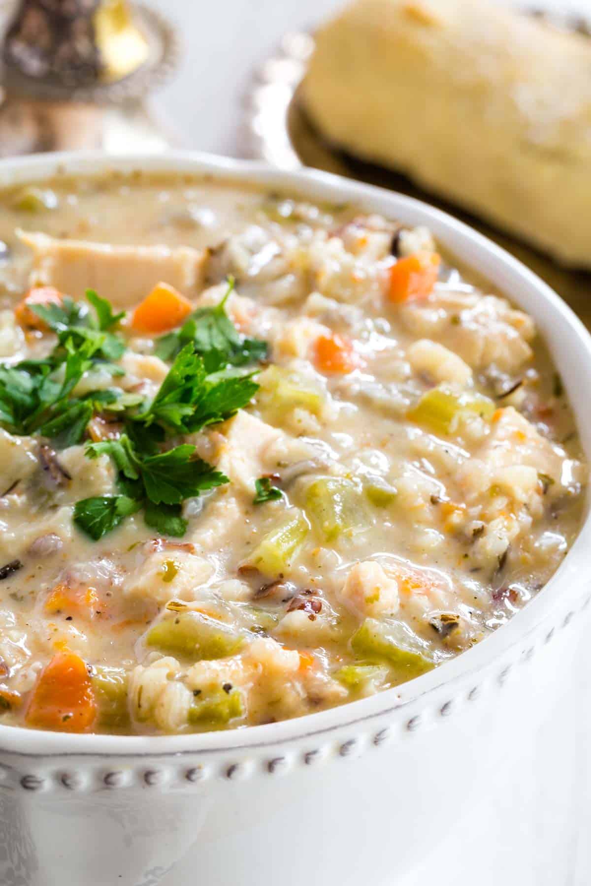 A bowl full of chicken wild rice soup garnished with fresh parsley.