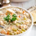 A bowl full of chicken wild rice soup garnished with fresh parsley.