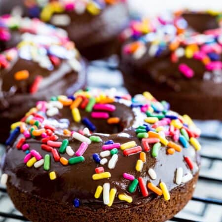 Glazed and decorated gluten-free chocolate donuts on a wire rack.