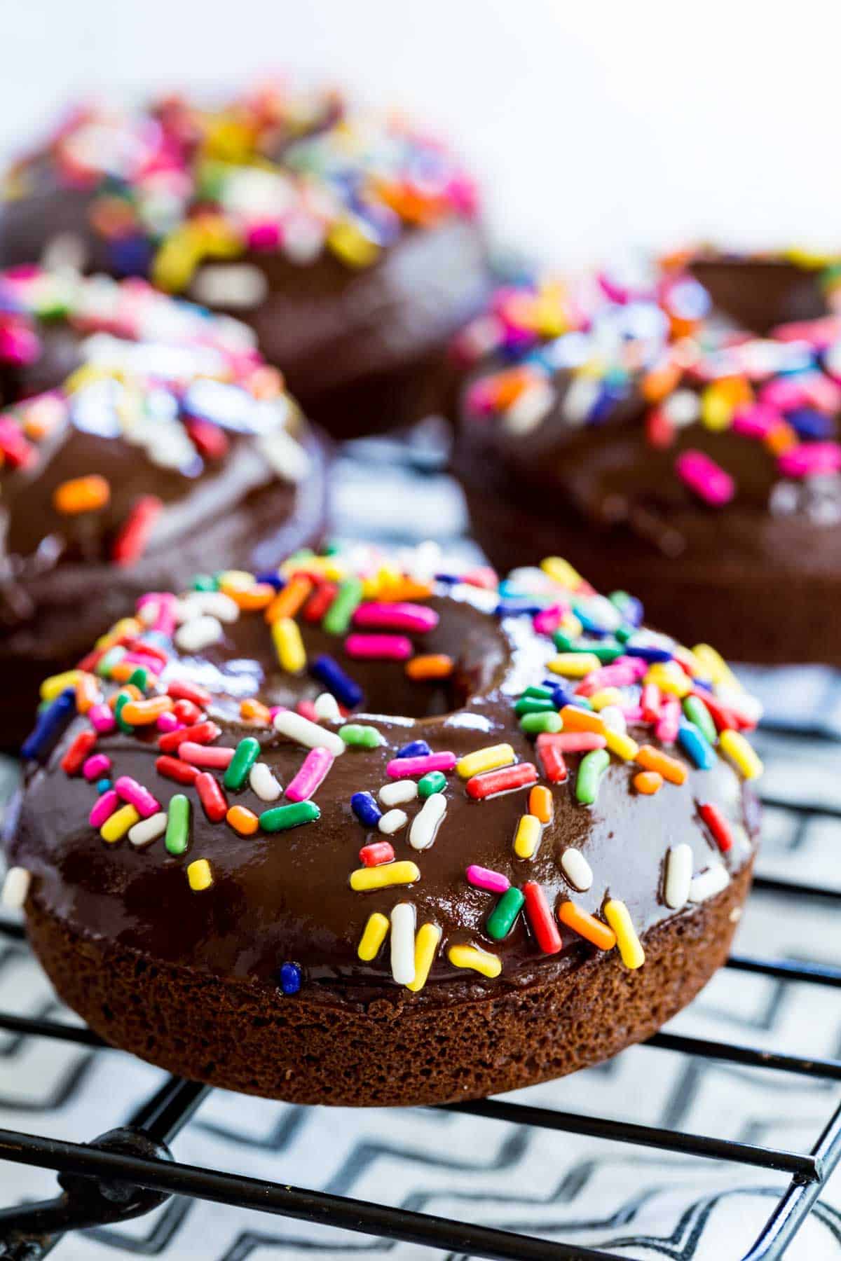 Glazed and decorated gluten-free chocolate donuts on a wire rack.