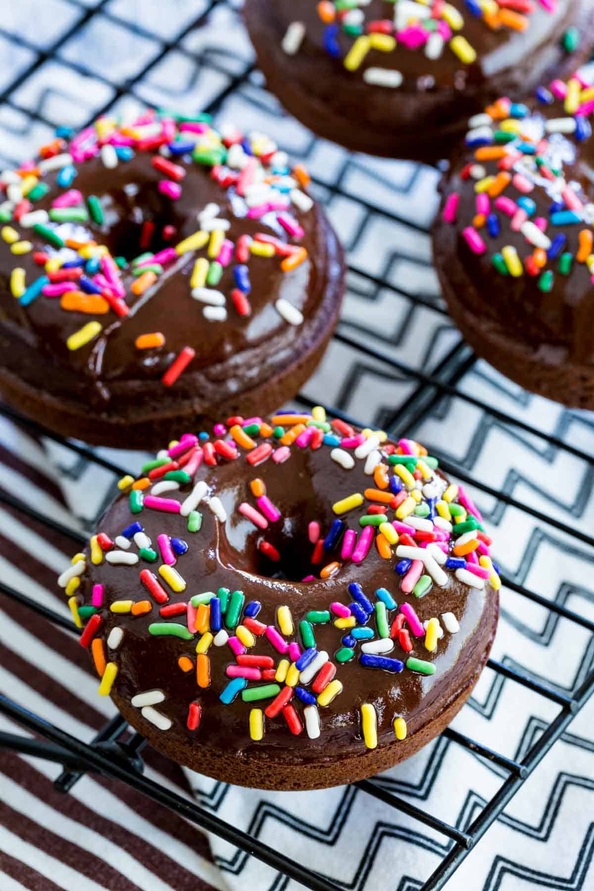 Glazed and decorated gluten-free chocolate donuts on a wire rack.