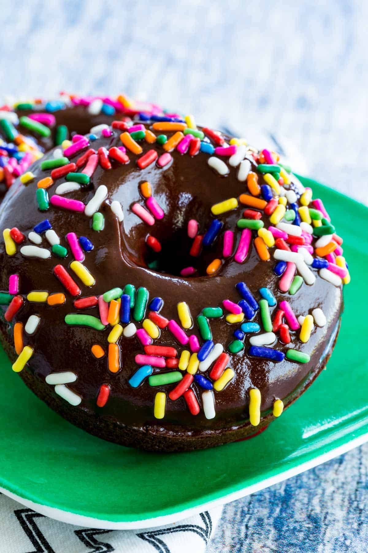Close up of a glazed gluten-free chocolate donut covered in rainbow sprinkles.