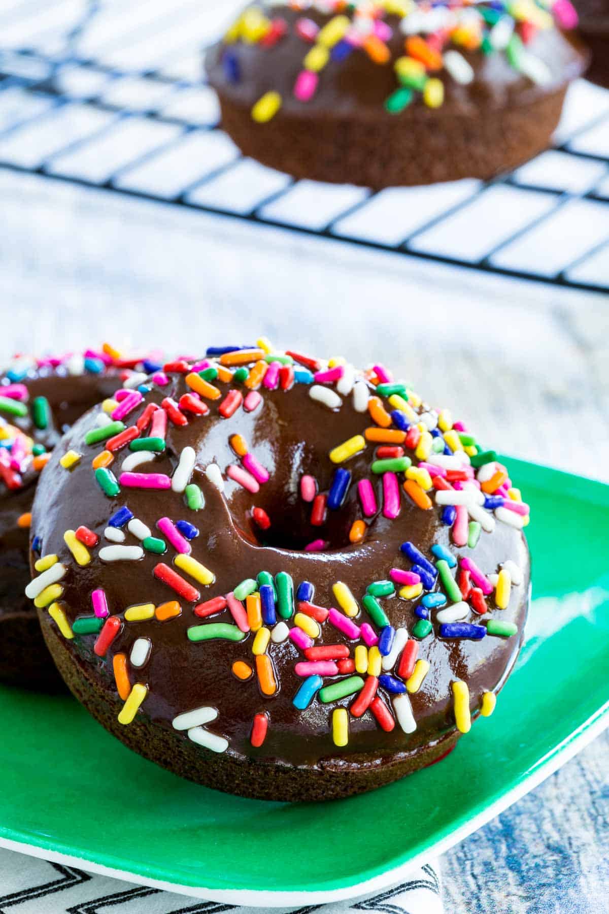 Gluten-free chocolate donuts covered in rainbow sprinkles, on a plate.