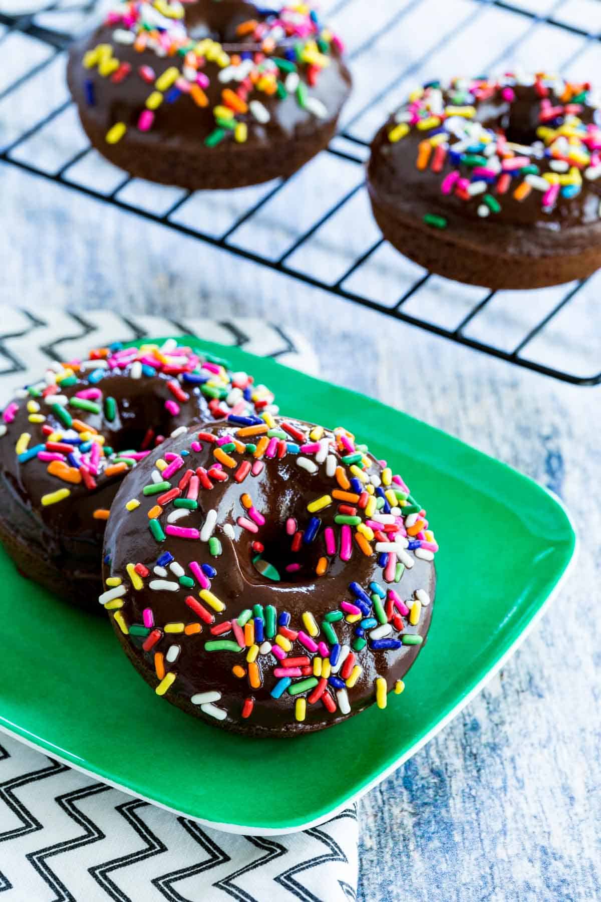 Chocolate-glazed gluten-free chocolate donuts covered in rainbow sprinkles.