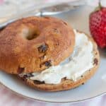 A close-up shot of a cinnamon raisin bagel with cream cheese spread onto the bottom half