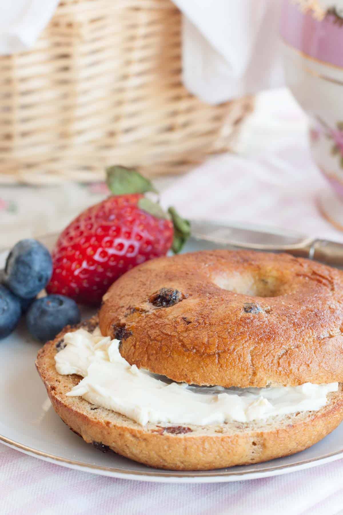 A cinnamon raisin bagel with cream cheese on a plate beside some fresh berries