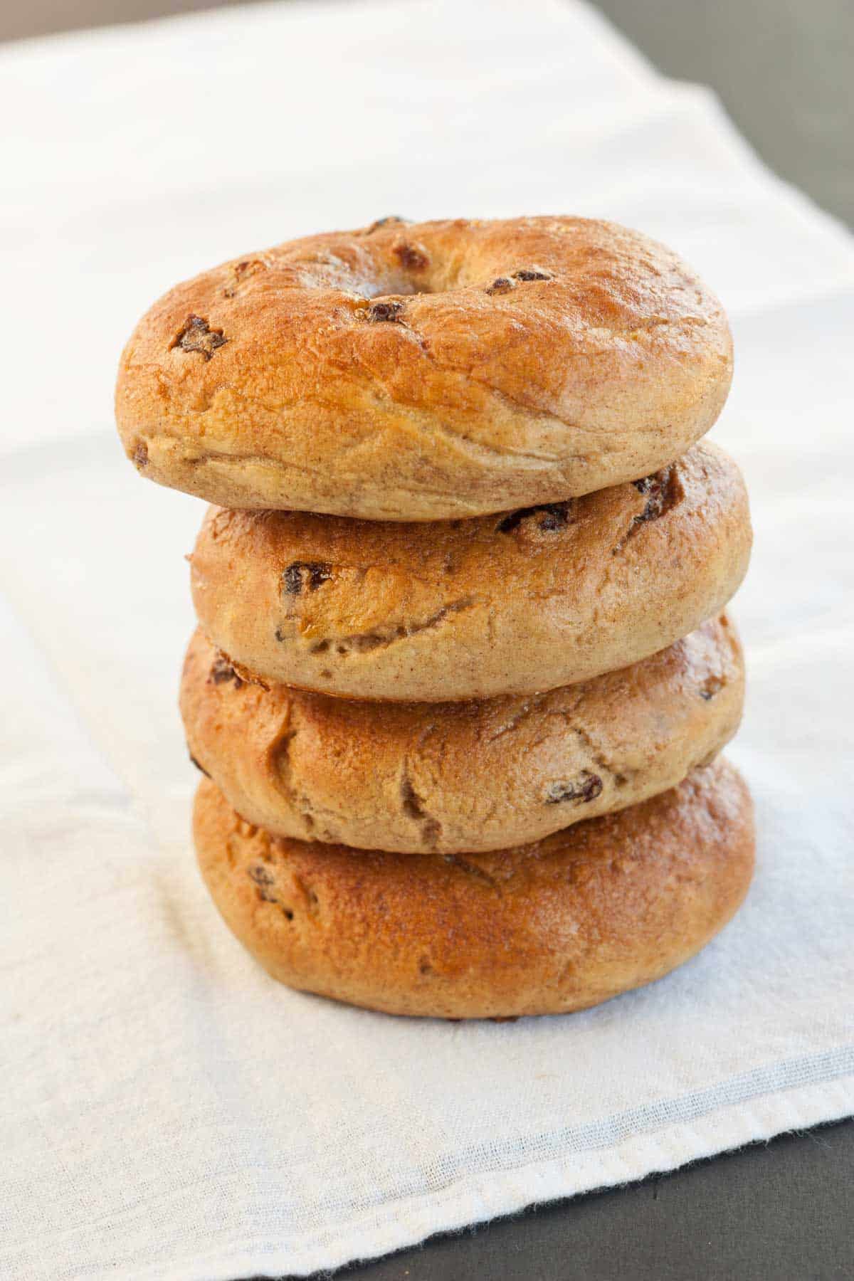 Four cinnamon raisin bagels stacked on top of a large cloth napkin