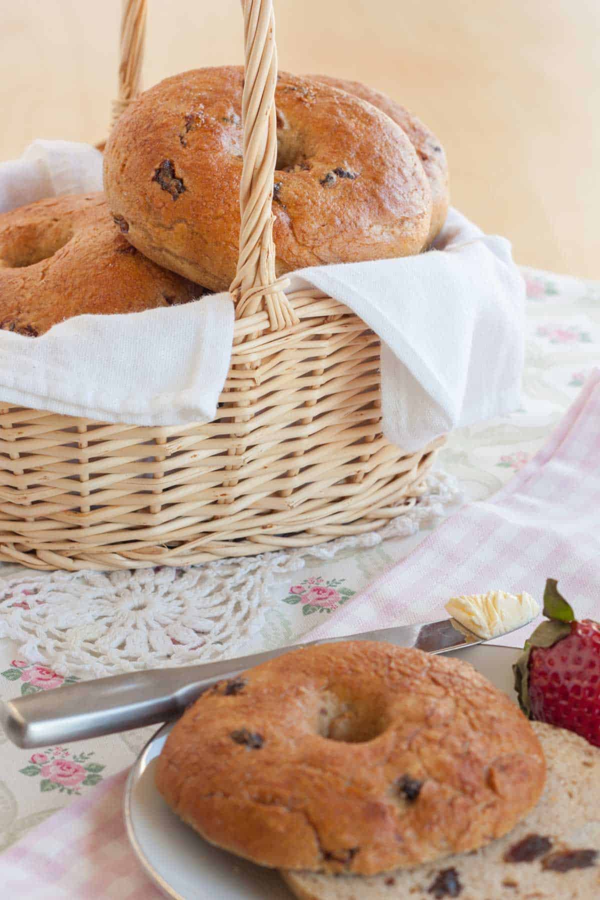 A wicker basket full of cinnamon raisin bagels with a halved bagel and a butter knife in the foreground