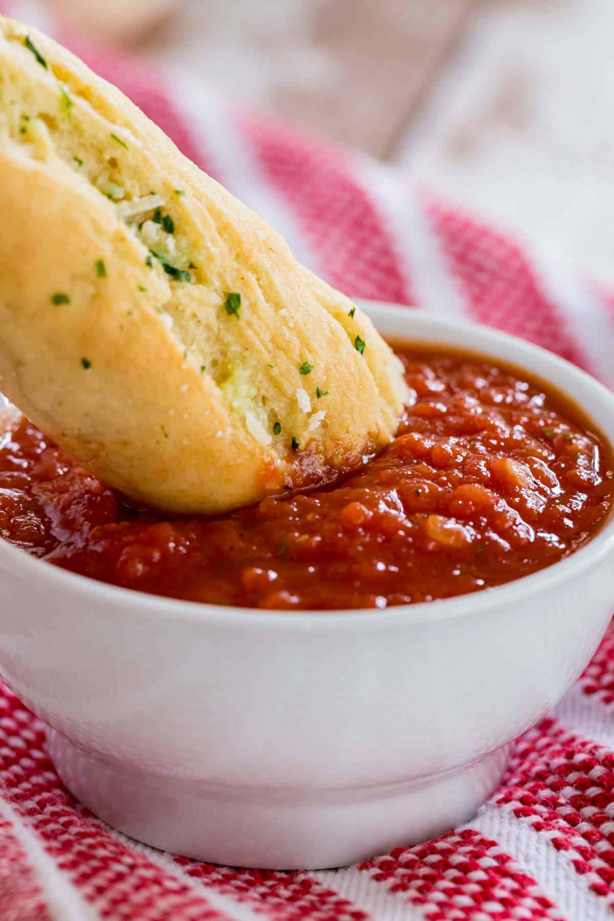 A breadstick being dunked into a bowl of marinara sauce.