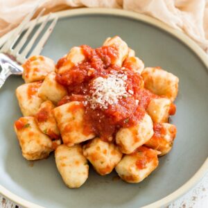 A plate of gnocchi with tomato sauce and a sprinkle of parmesan cheese.