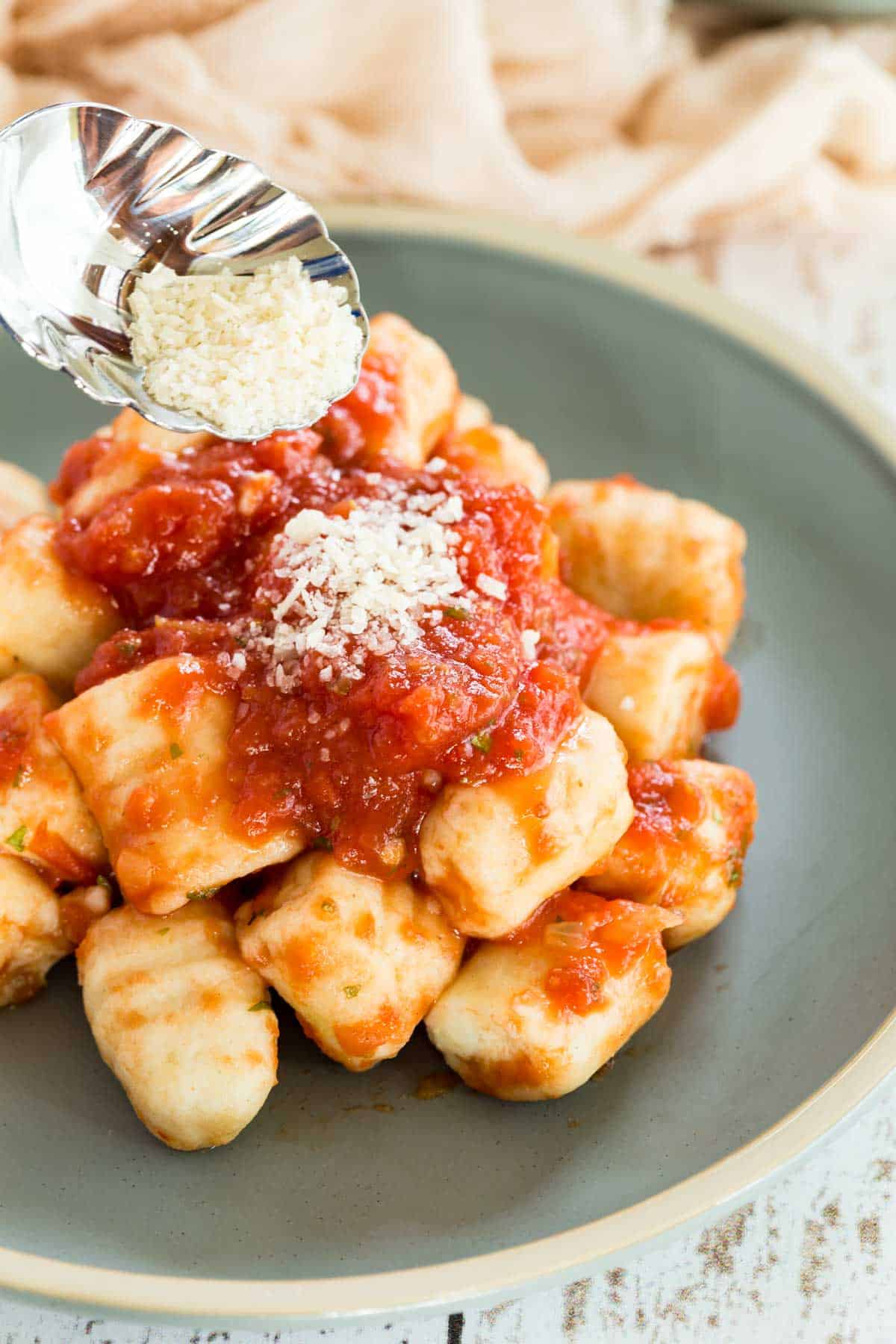 Gluten-free gnocchi and tomato sauce is sprinkled with a spoonful of parmesan cheese.