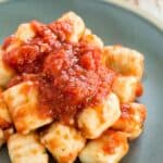 Homemade gnocchi covered in tomato sauce on a plate.