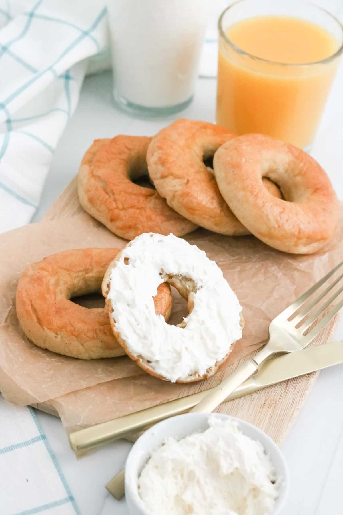 Gluten free bagels with one cut in half and smeared with cream cheese, on a wooden serving tray