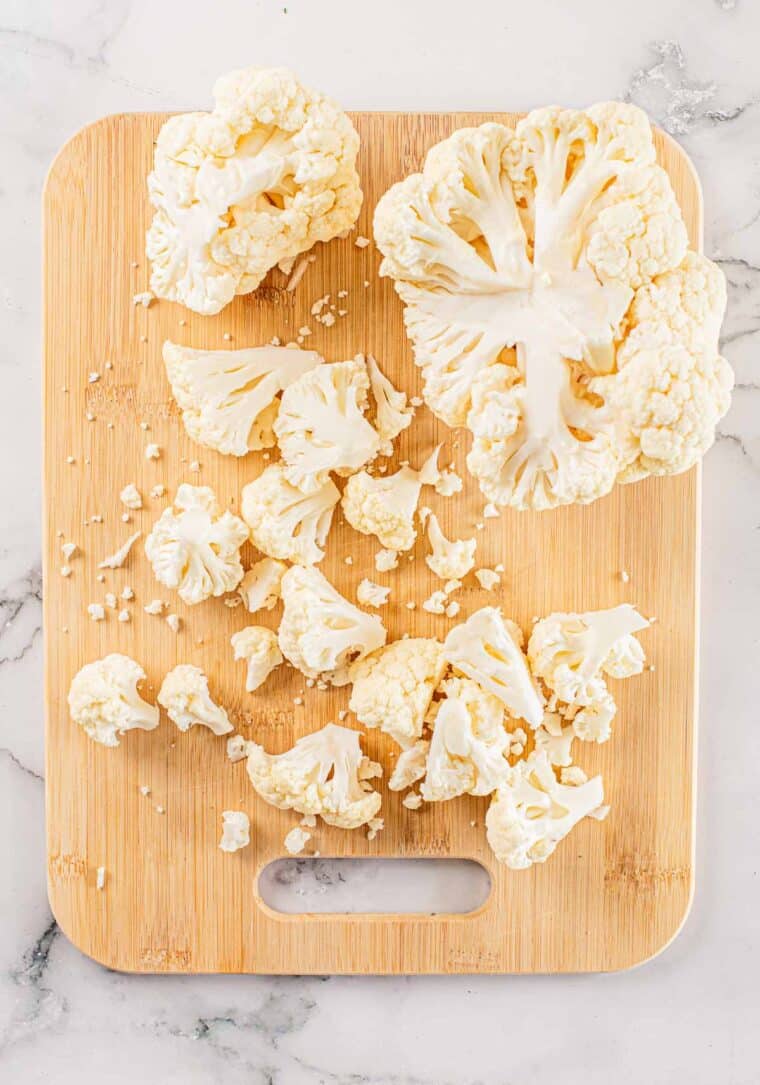 a head of cauliflower on a cutting board being cut into florets