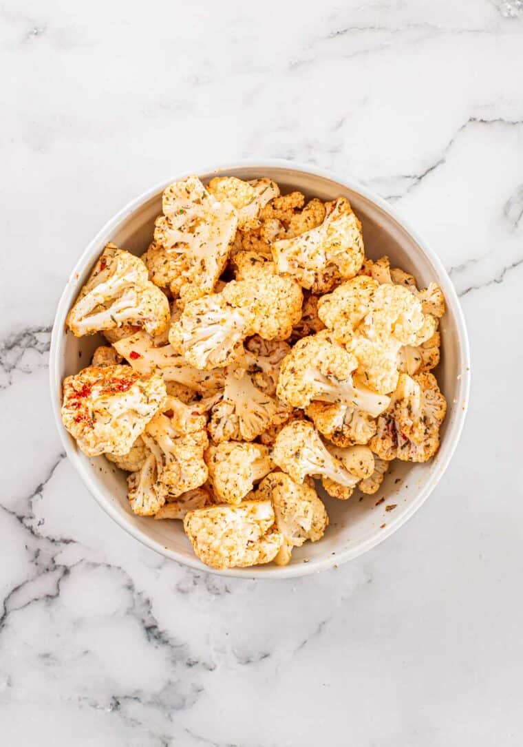 raw cauliflower florets in a bowl coated in seasonings
