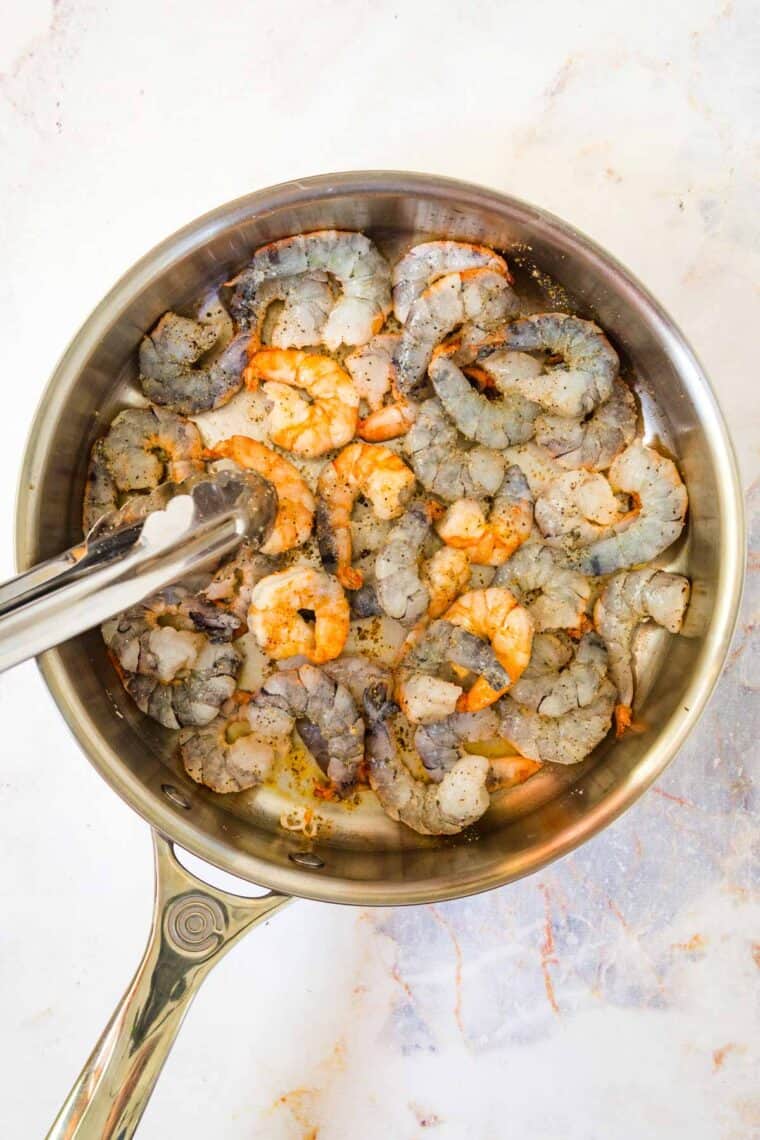 shrimp being flipped with tongs in a skillet as it cooks