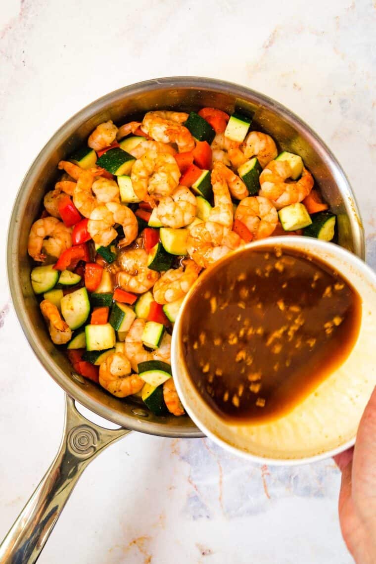 pouring the sauce mixture into the skillet with the shrimp and vegetables