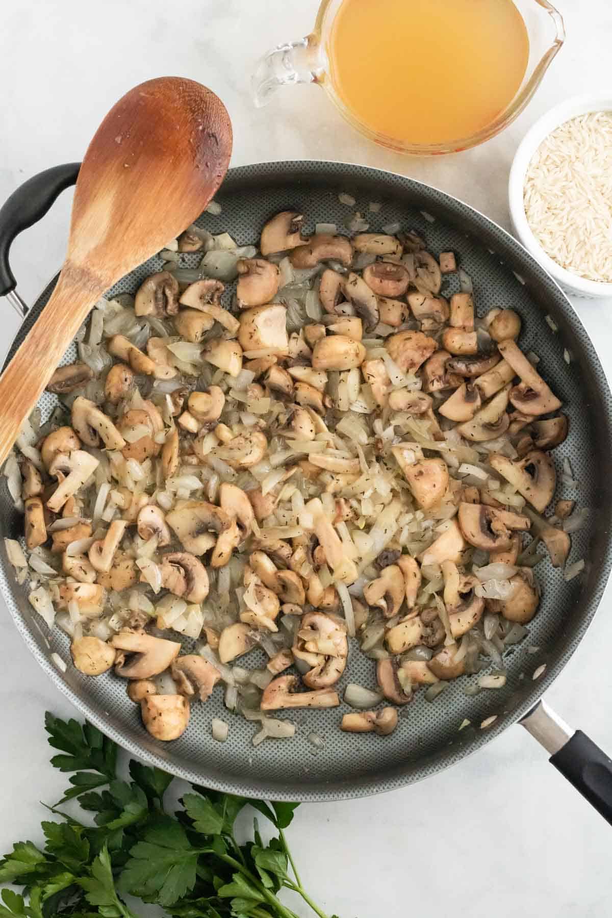 Mushrooms are sautéed in a skillet with onions.