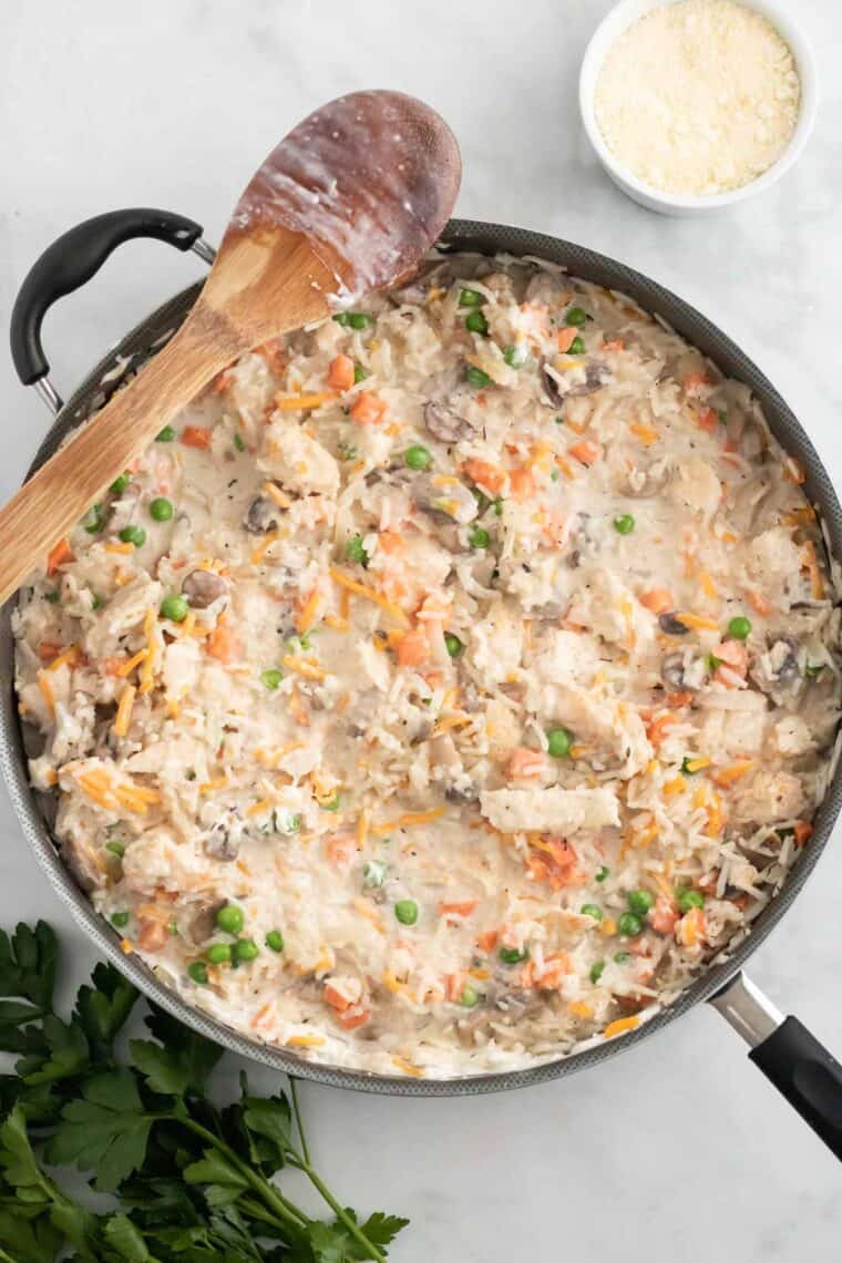 Vegetables and chicken are added to a skillet with creamy rice.