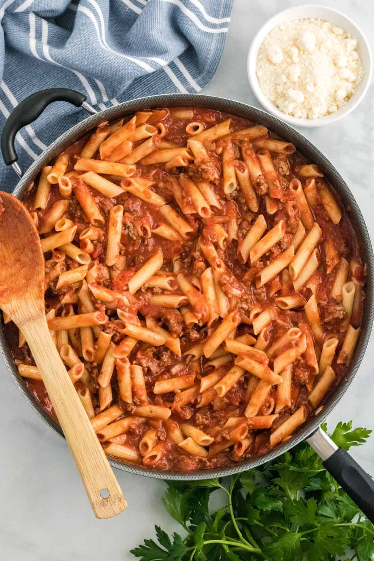 Ziti pasta added to meat sauce in a skillet.