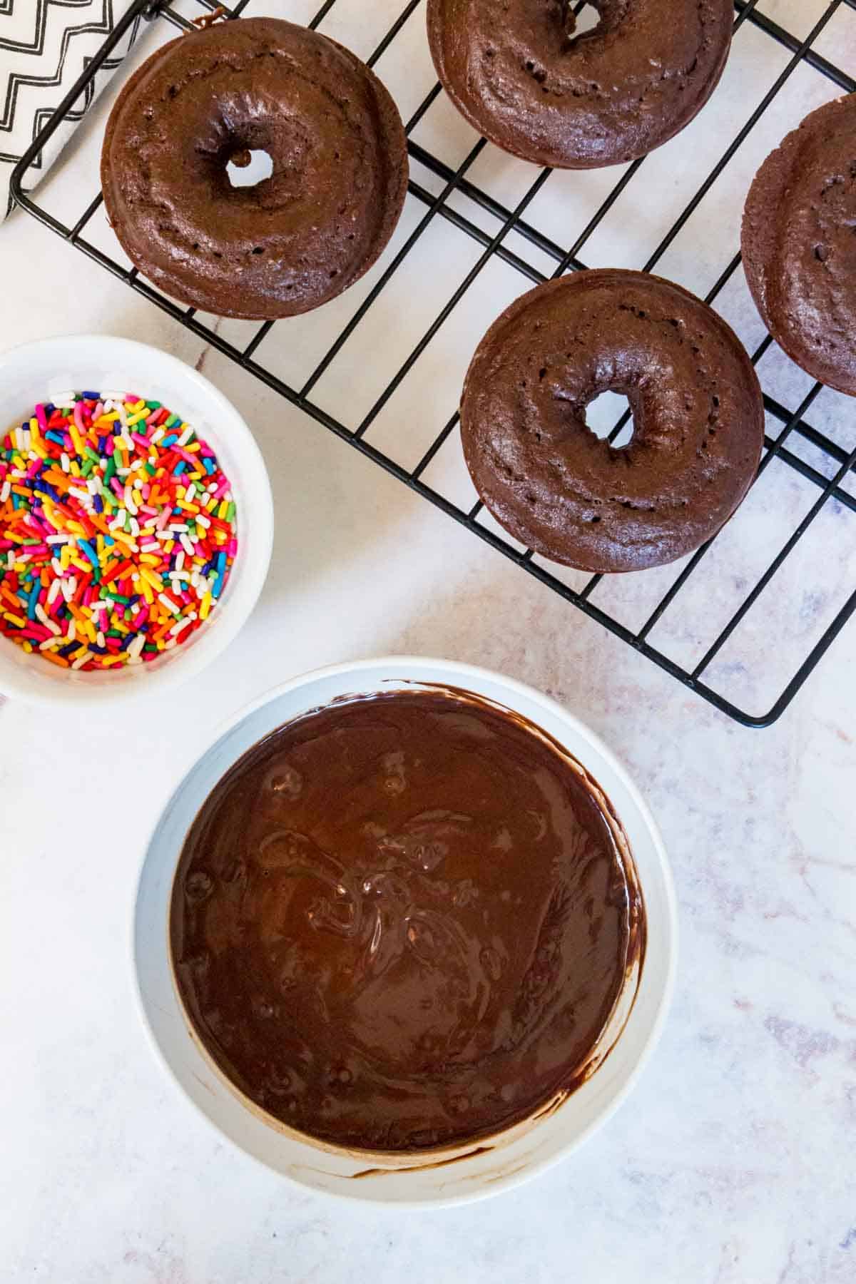 Chocolate donuts on a wire rack, next to a bowl of chocolate glaze.