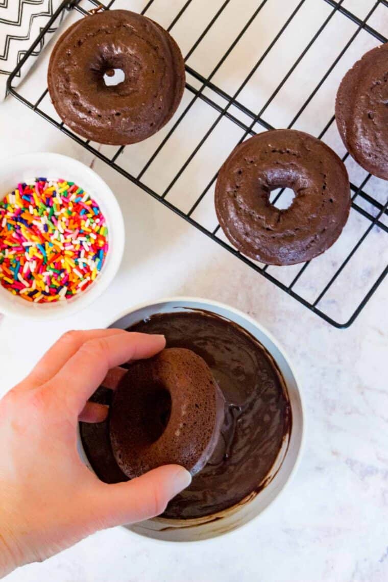 Gluten-free chocolate donuts are dipped into a melted chocolate glaze.