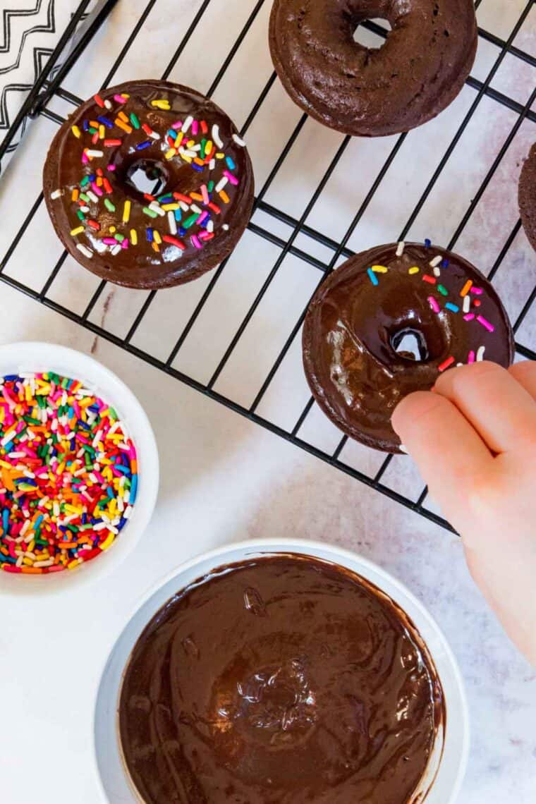 Rainbow sprinkles are added on top of glazed chocolate donuts.