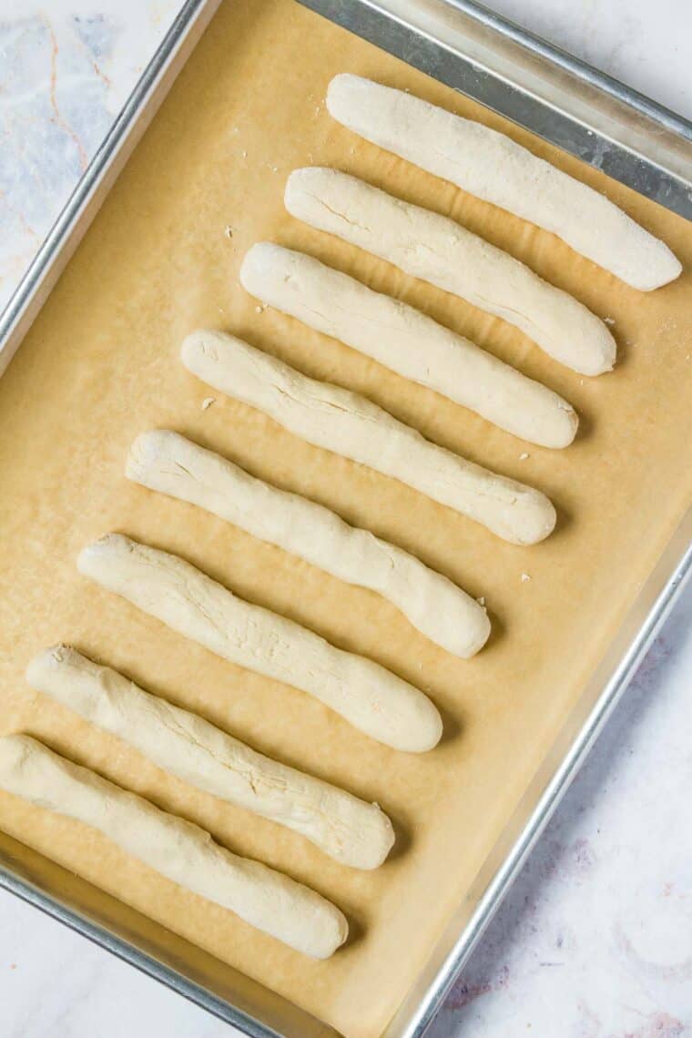 Dough rolled into breadsticks on a parchment-lined baking sheet.