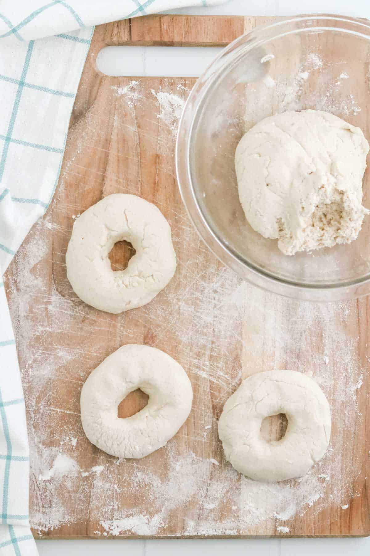 Dough being rolled into bagel shapes on a floured surface.