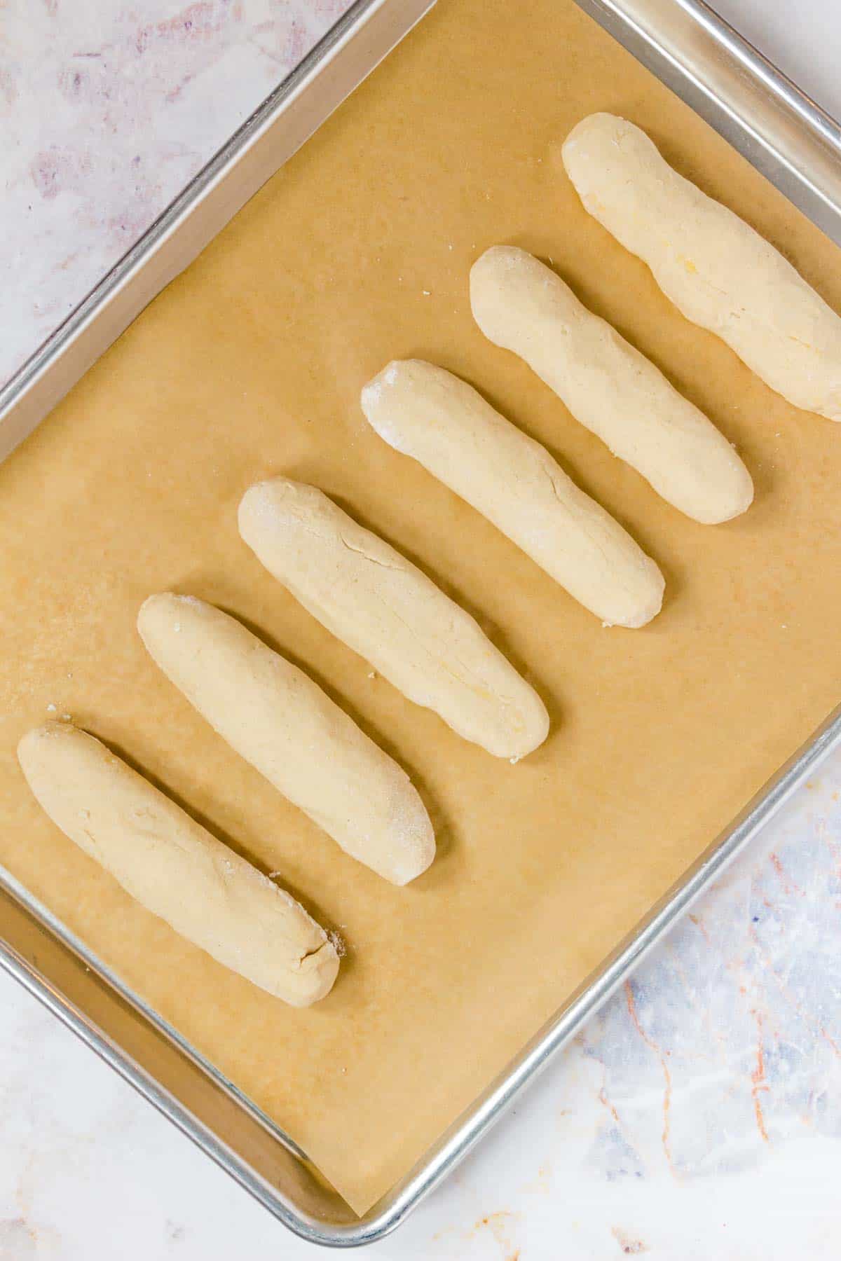 A row of rolled, unbaked breadstick dough on a baking tray.