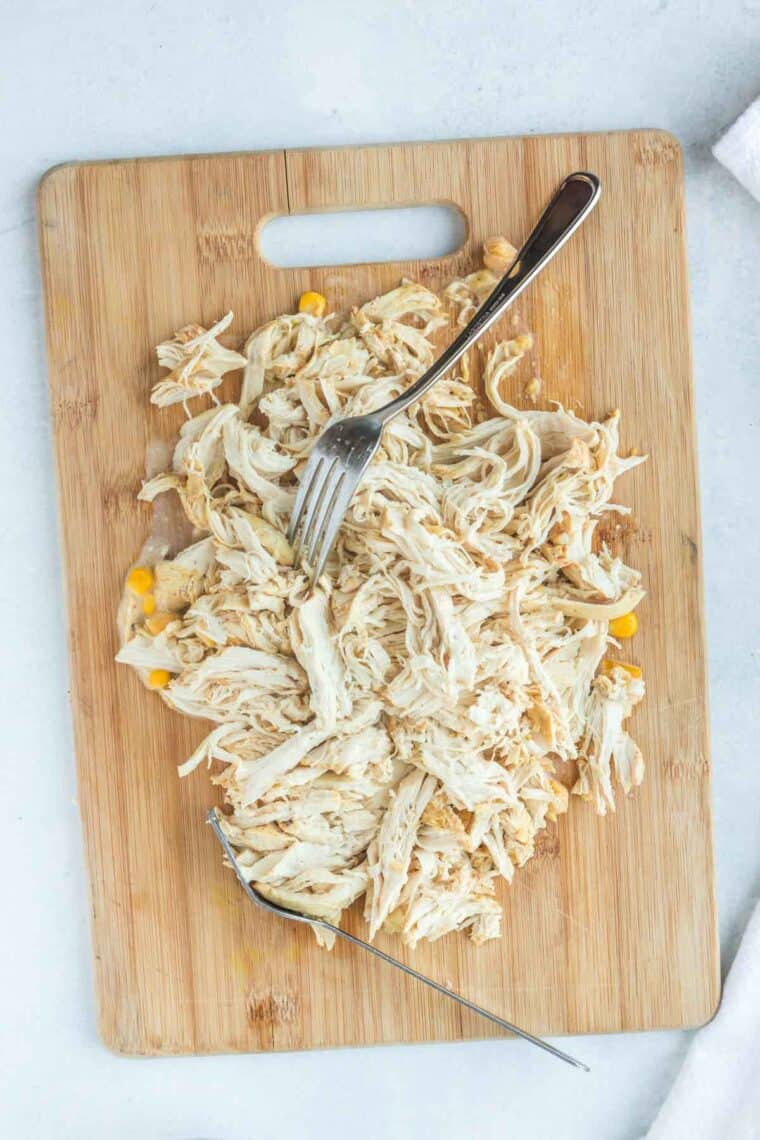 chicken being shredded with two forks on a cutting board
