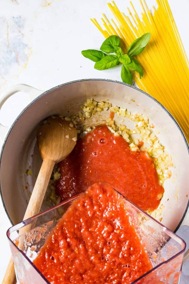 Tomato puree is added to a pot with onion and garlic.