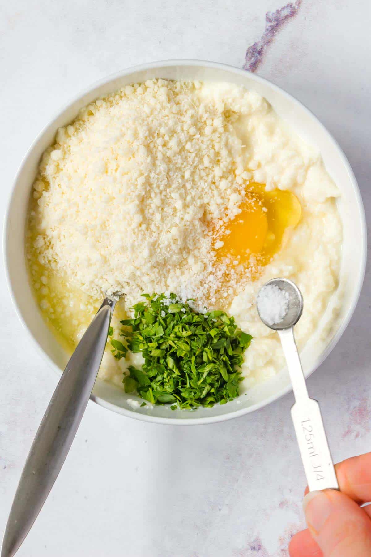 Parmesan cheese, an egg, chopped parsley and the remaining ingredients for the ricotta filling inside of a bowl