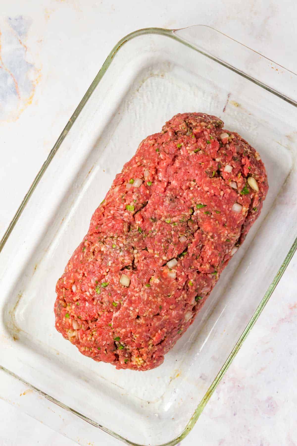 The sealed raw meatloaf inside of a large glass baking dish