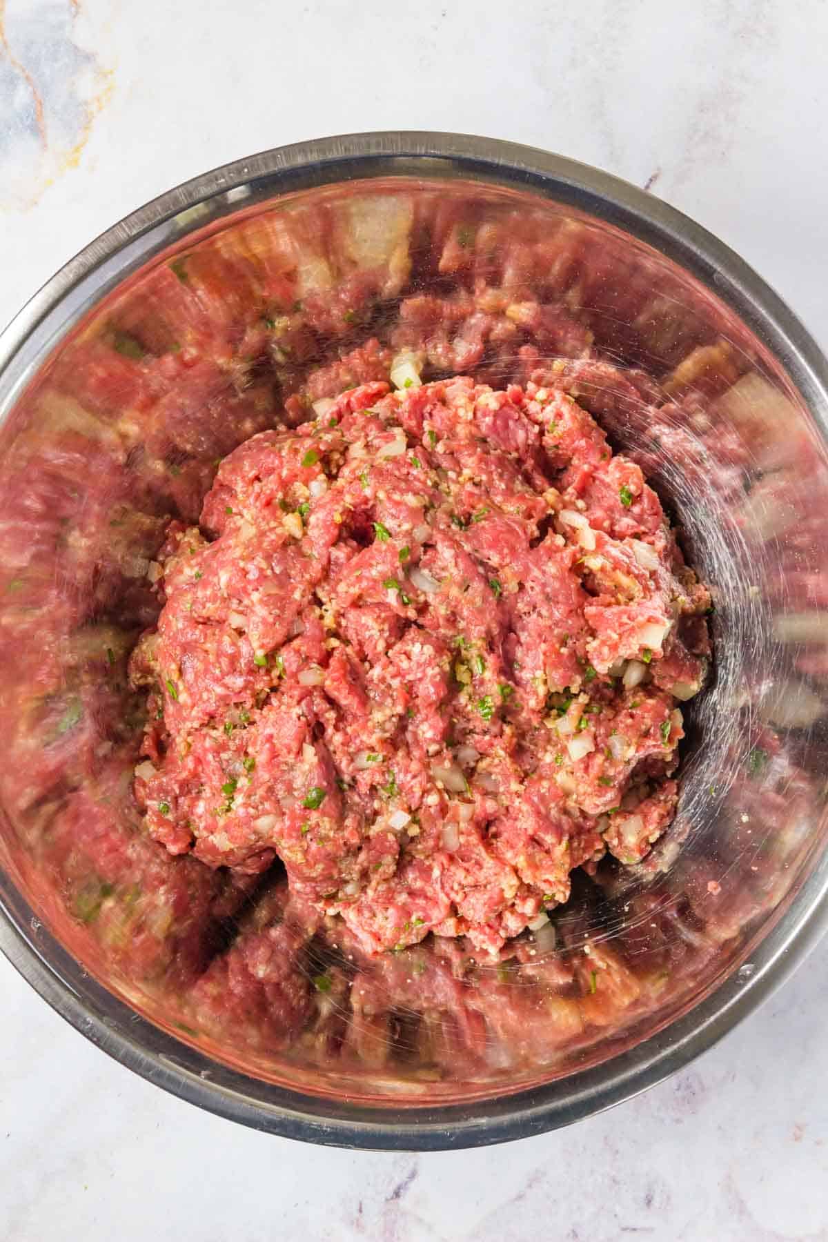 The prepared beef mixture inside of a large metal mixing bowl on a countertop