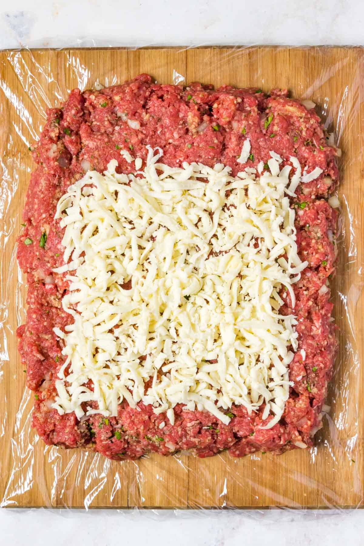 The beef mixture shaped into a rectangle with shredded parmesan cheese spread on top of it