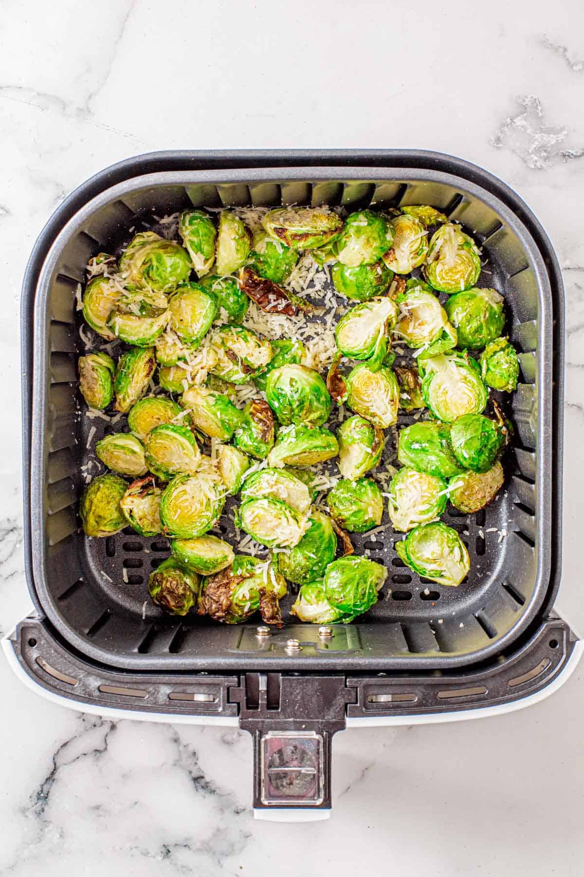 partially cooked Brussels sprouts in an air fryer basket sprinkled with parmesan cheese