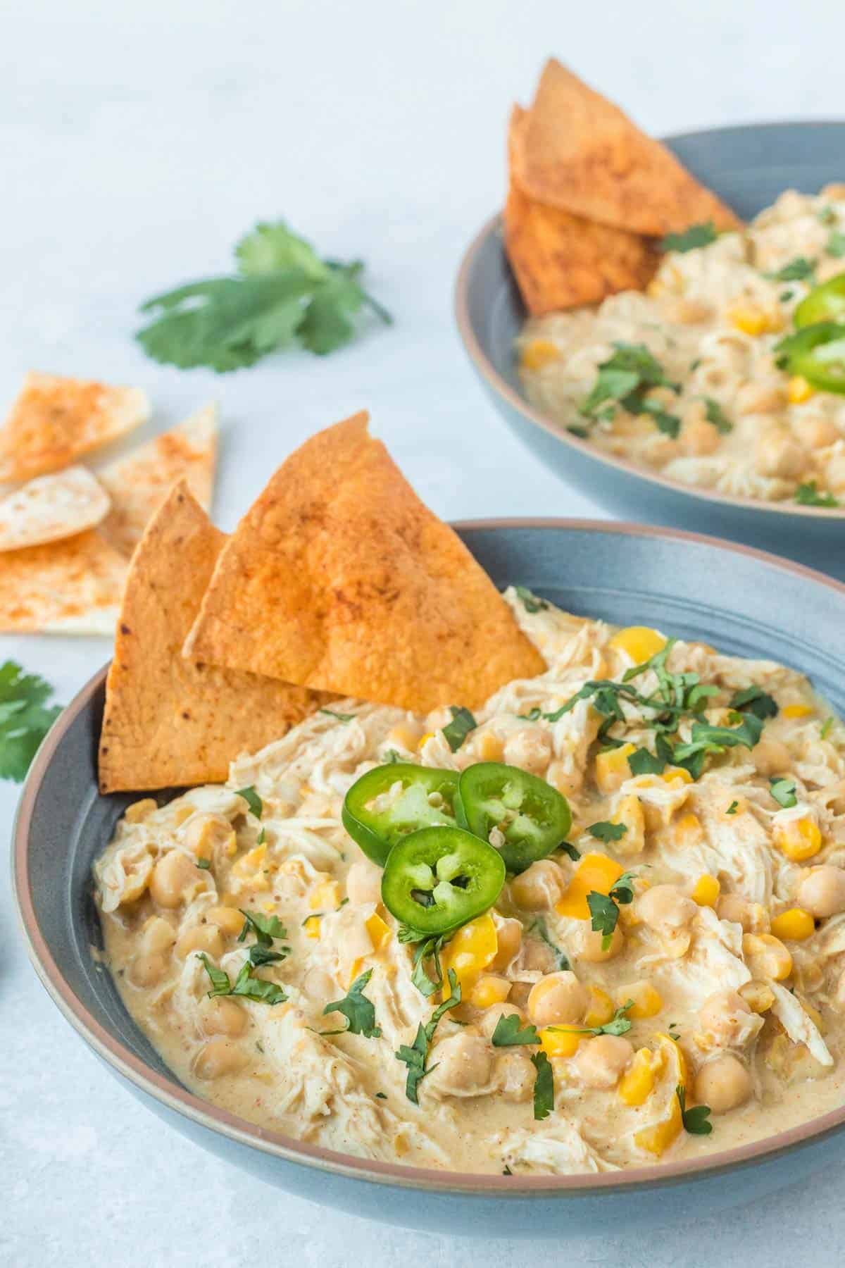 White chicken chili in a blue bowl with cilantro, jalapeno slices, and tortilla chips on top.