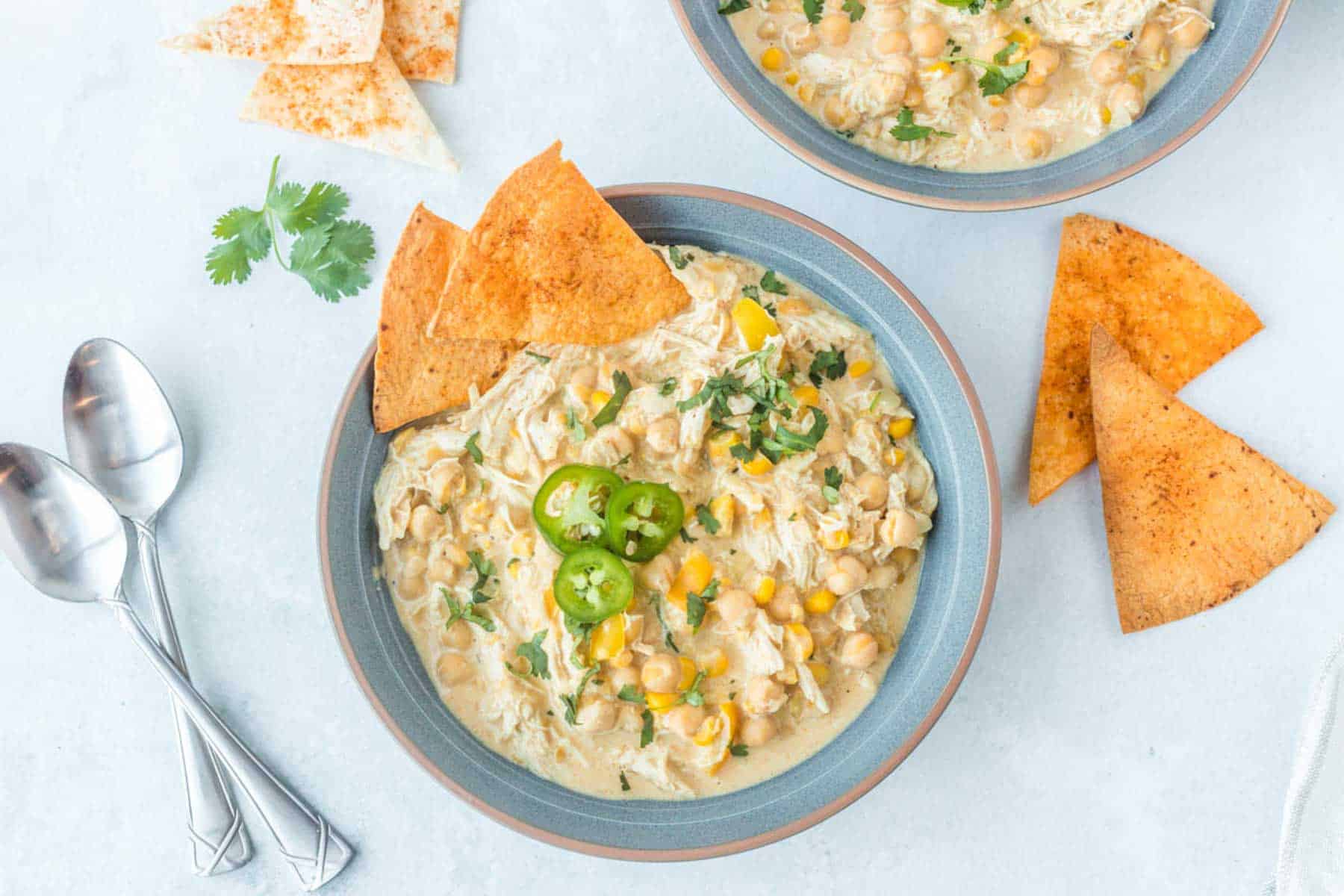 a bowl of white chicken chili with two spoons and tortilla chips