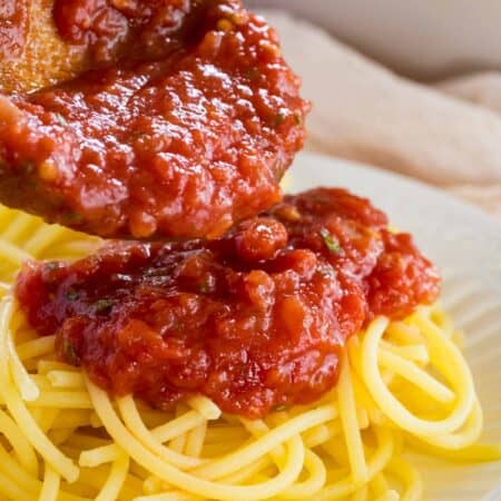 Marinara sauce is spooned over top a bed of spaghetti noodles.