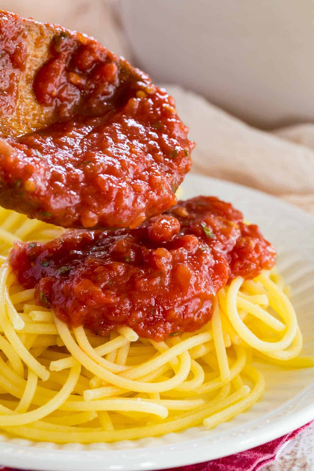 Marinara sauce is spooned over top a bed of spaghetti noodles.