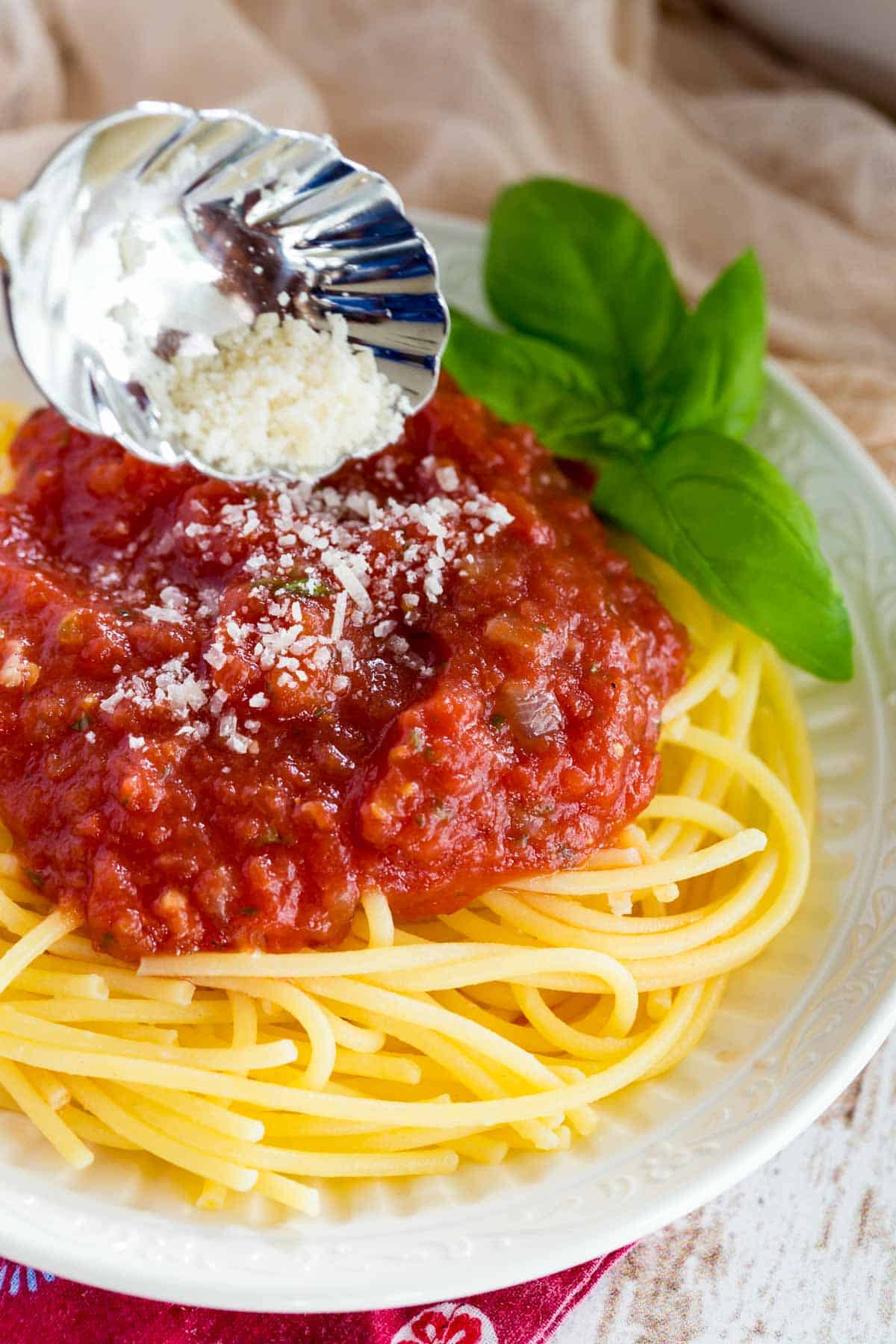 Parmesan cheese is sprinkled over spaghetti with marinara sauce.